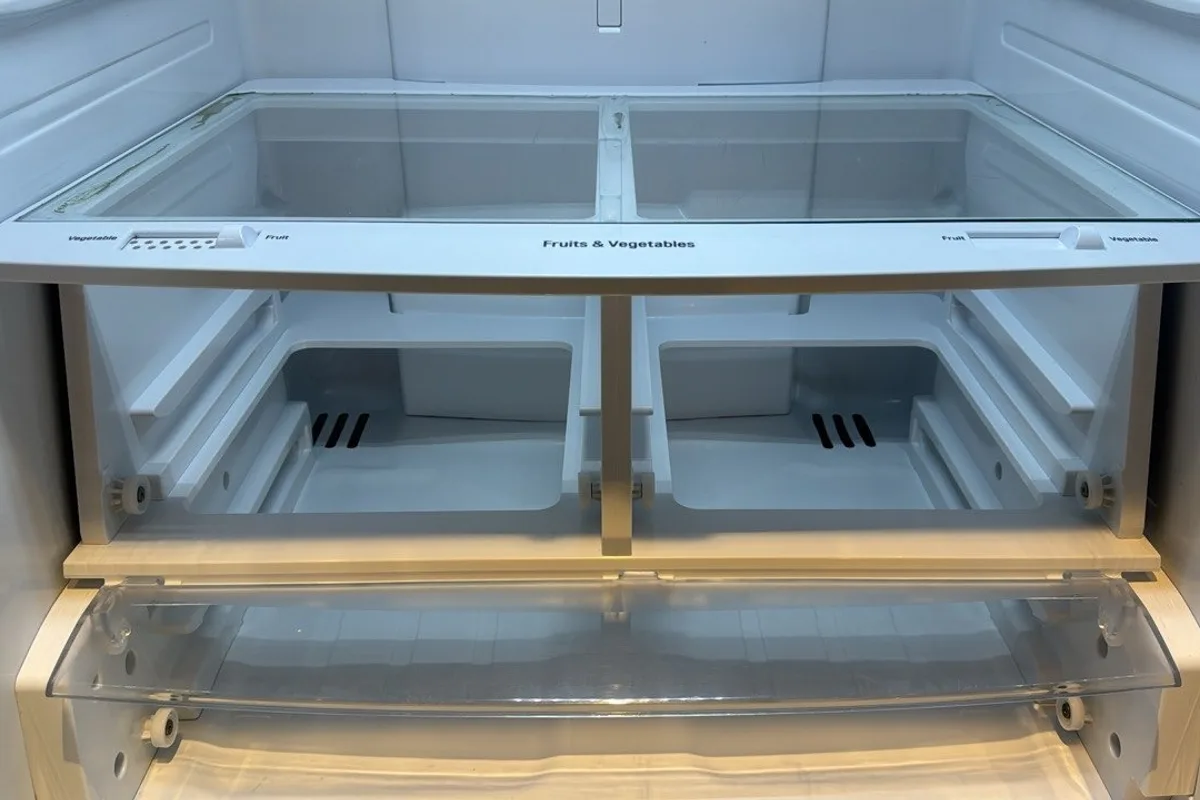 Empty fridge with both crisper drawers taken out, the bays and the glass shelf above them wiped clean