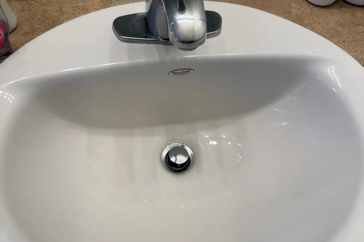 White bathroom sink with a chrome faucet and drain, on a beige counter