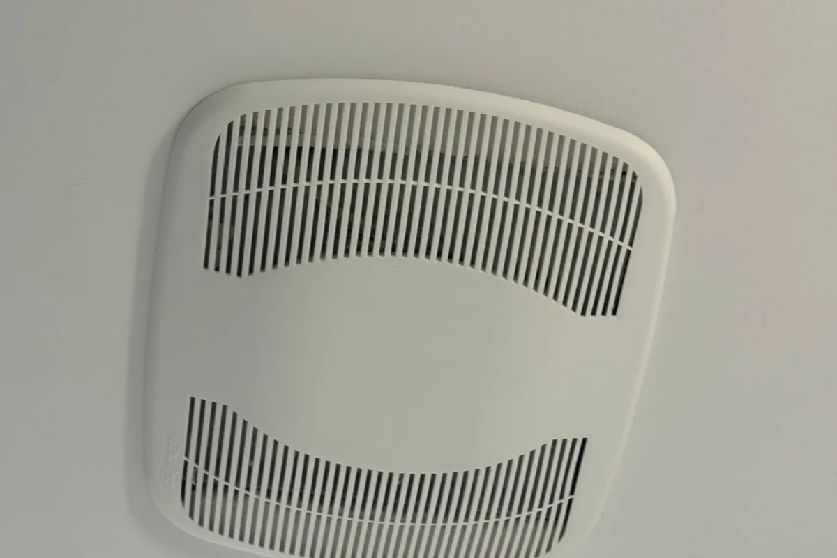 White plastic cover of a bathroom ceiling fan on a white ceiling