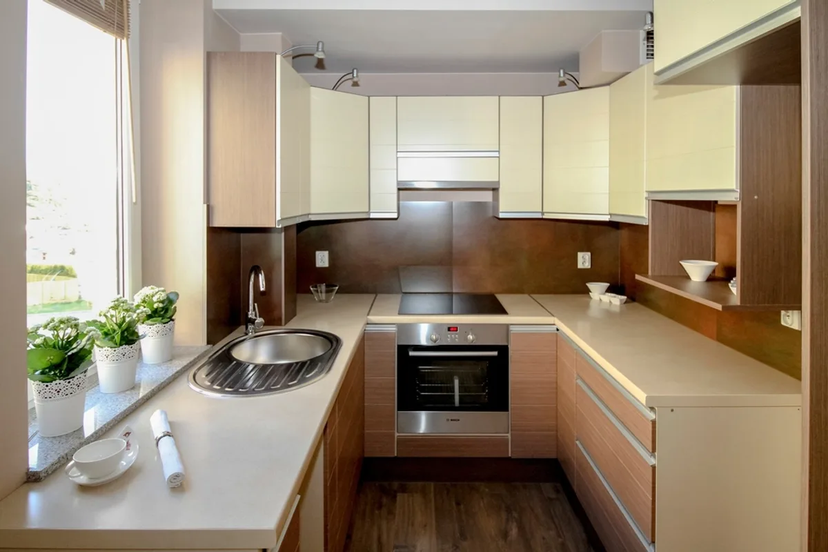 Small U-shaped kitchen with light cabinets, a round steel sink by a window and a built-in oven
