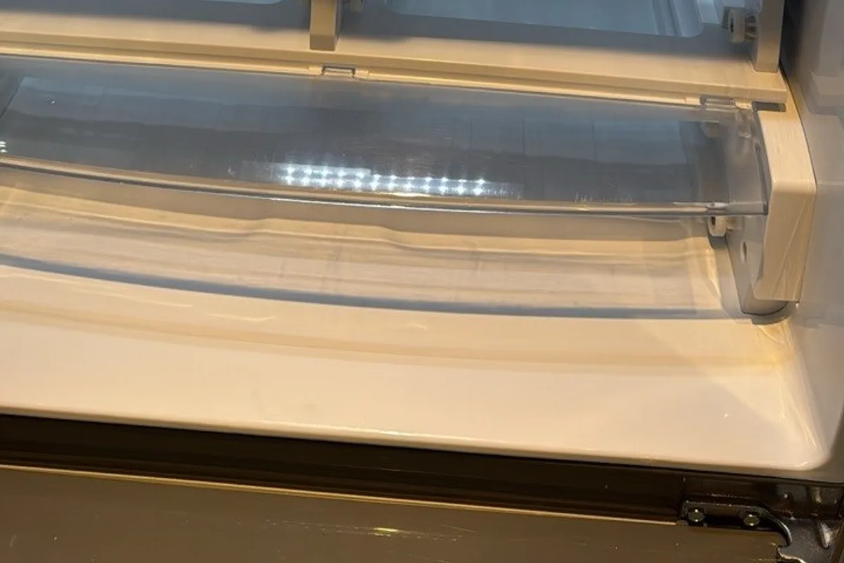 Clear bottom drawer and white floor of an empty fridge, lit from inside
