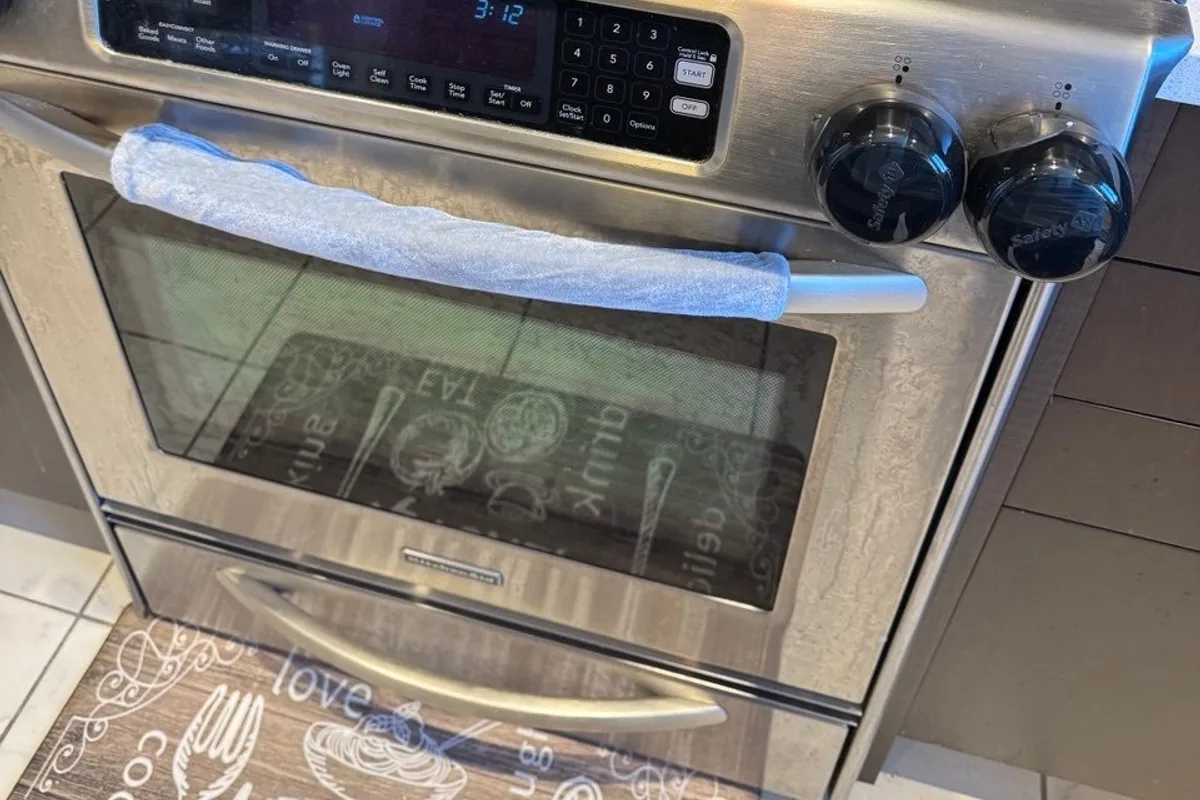 Stainless steel oven with a clean glass door, a handle wrapped in a blue cover and two knobs with safety caps