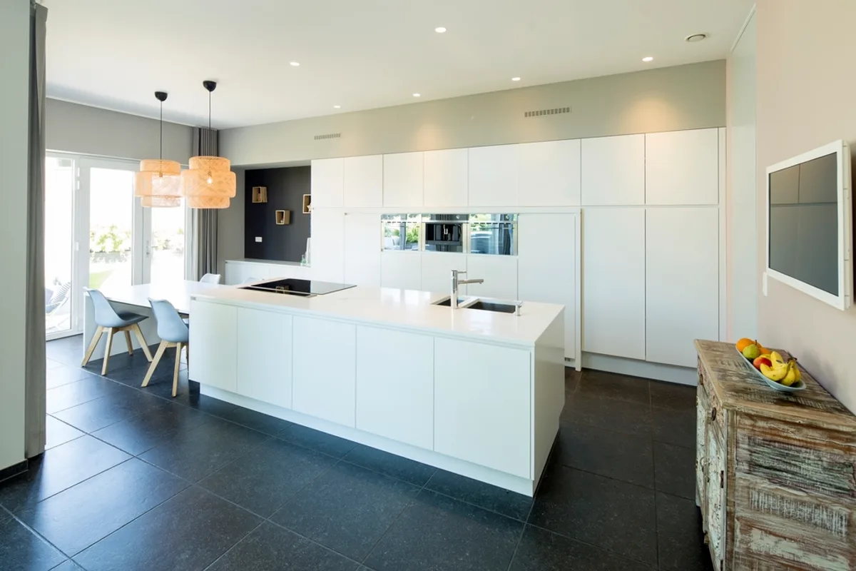 Large white kitchen with an island, a sink, built-in cabinets and two pendant lamps over a table