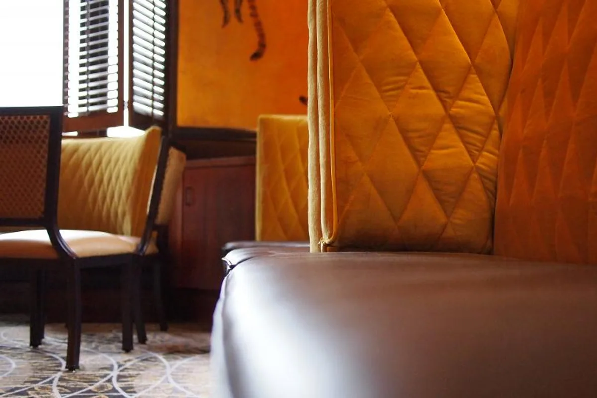 Restaurant booth with a quilted mustard fabric back and a brown leather seat, a chair and a patterned carpet beside it