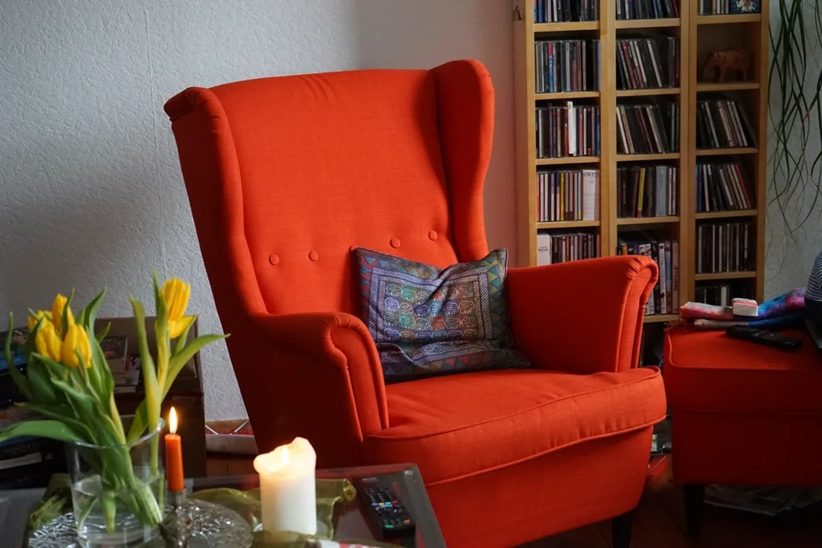 Orange fabric wingback armchair with a patterned cushion, next to a matching footstool and a bookcase