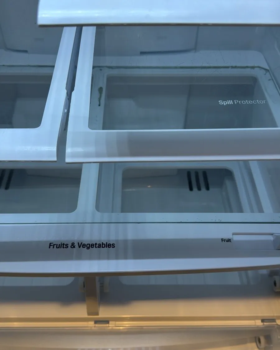 Glass fridge shelves pulled forward above two empty crisper drawers