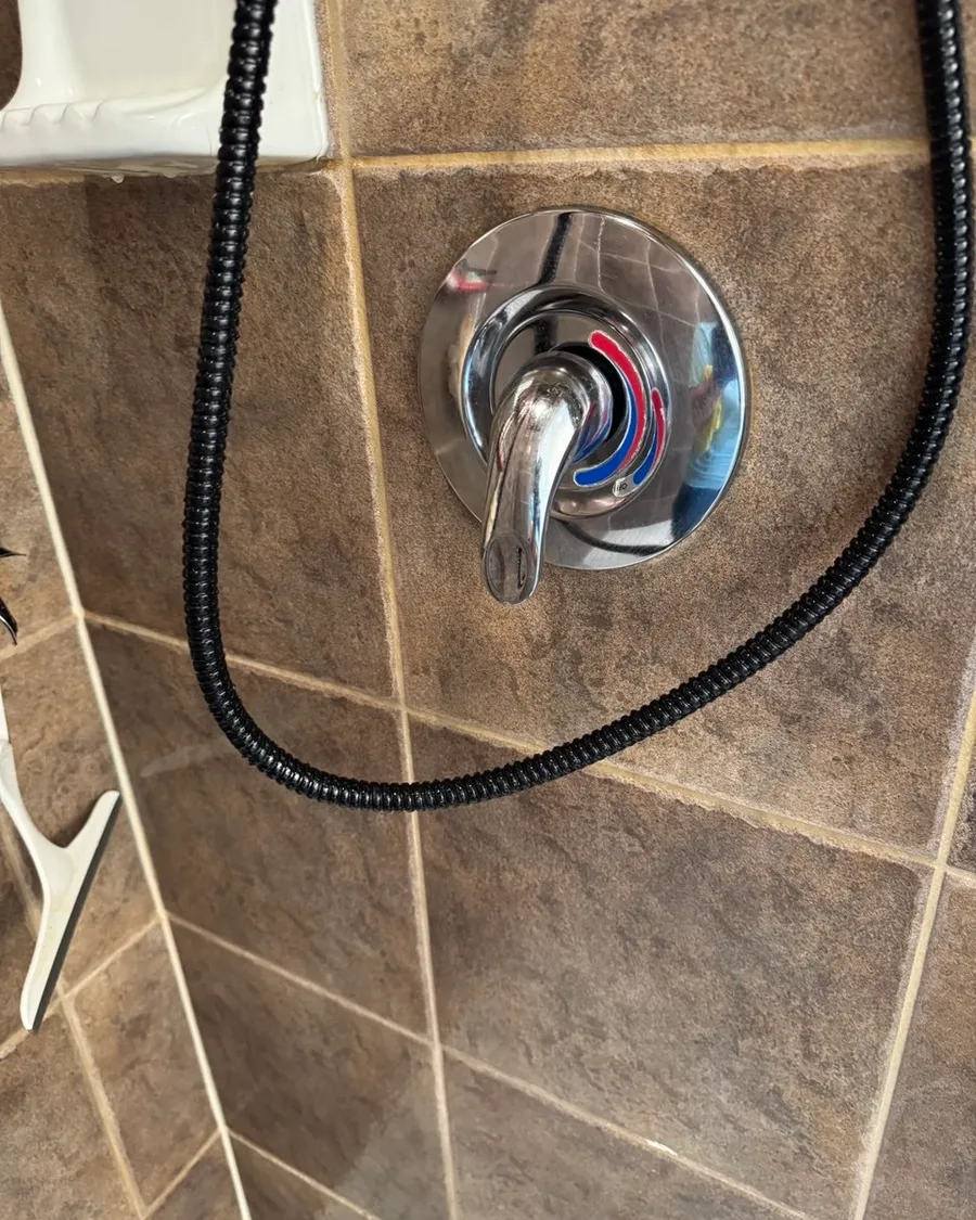 Chrome shower handle and a black hose on brown wall tile
