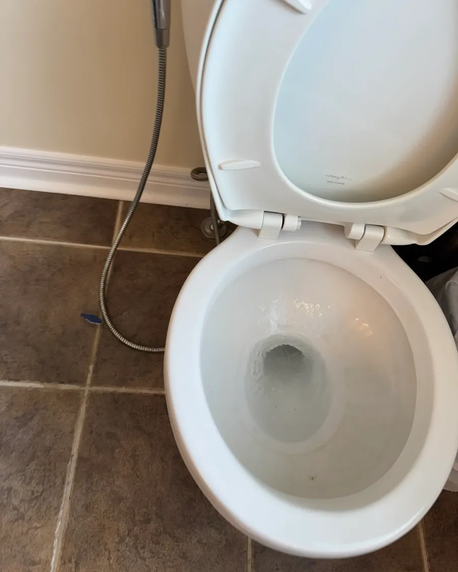 White toilet with the lid up and a clean bowl on a brown tile floor
