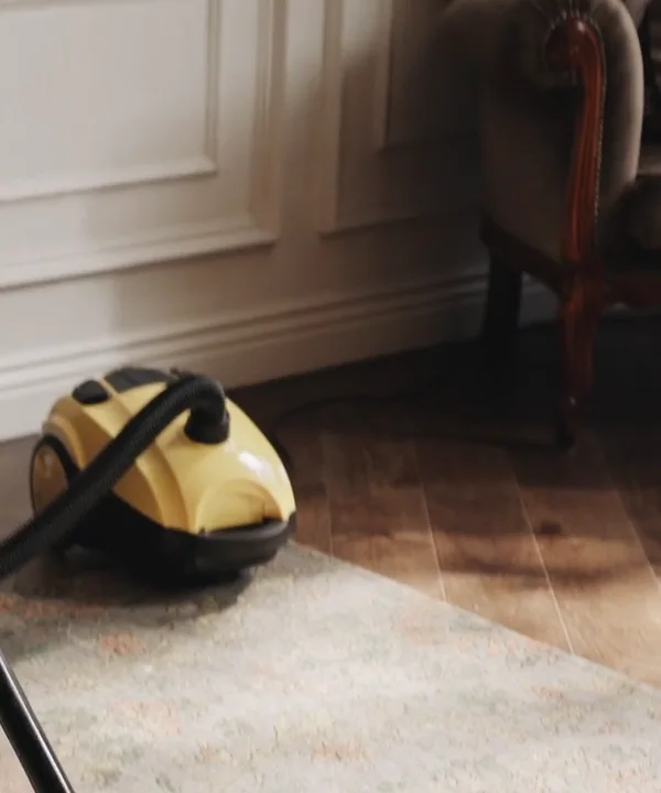 Yellow canister vacuum on a rug next to a wood floor